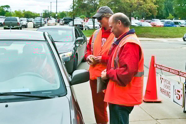 two parking attendants in orange vest talking to the car driver