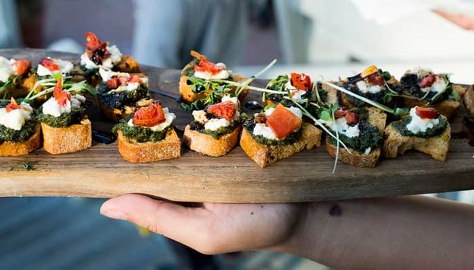 a hand holding a wooden tray of bite size foods